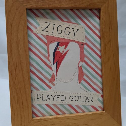 Image of a paper and stitch portrait of Ziggy Stardust. A simple portrait of ziggy startdust is flanked by tattoo style ribbon banners which read Ziggy Played Guitar