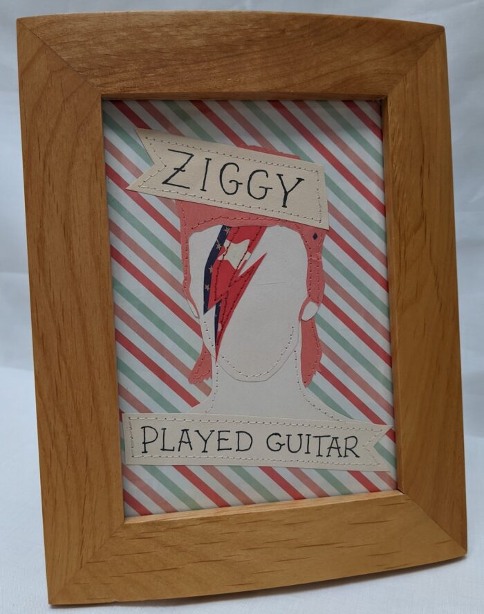 Image of a paper and stitch portrait of Ziggy Stardust. A simple portrait of ziggy startdust is flanked by tattoo style ribbon banners which read Ziggy Played Guitar